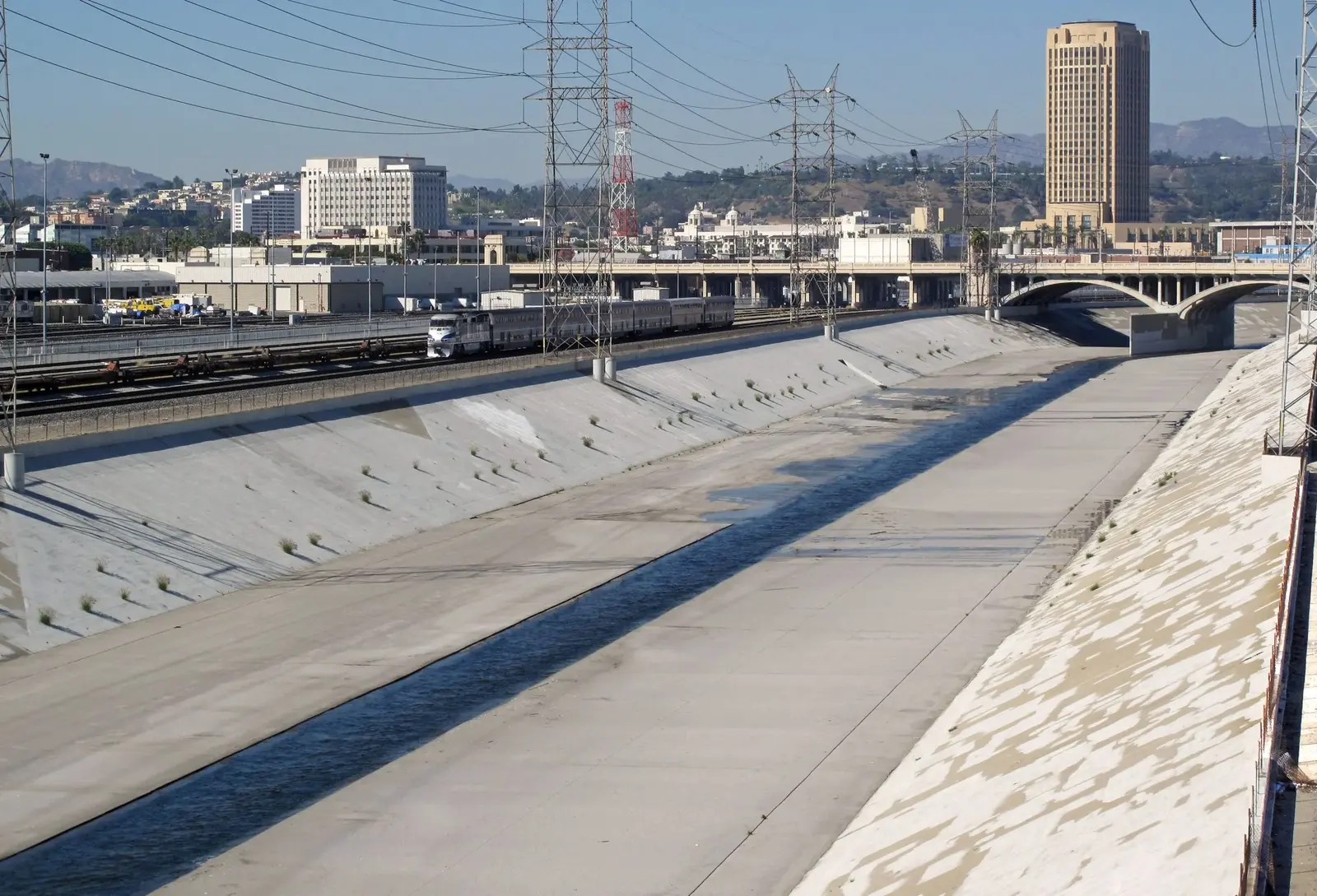 Concrete channel of the Los Angeles River with railway tracks, bridges and city buildings.